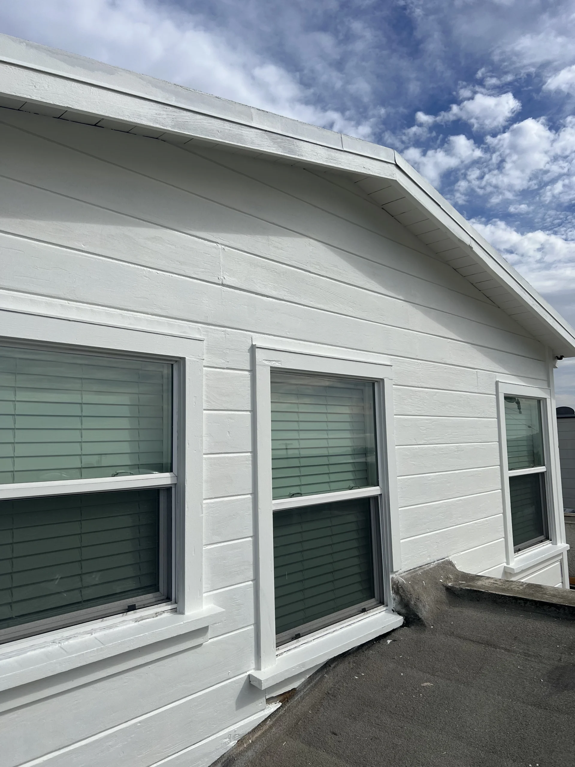 White building facade with three windows featuring green blinds, under a clear blue sky.