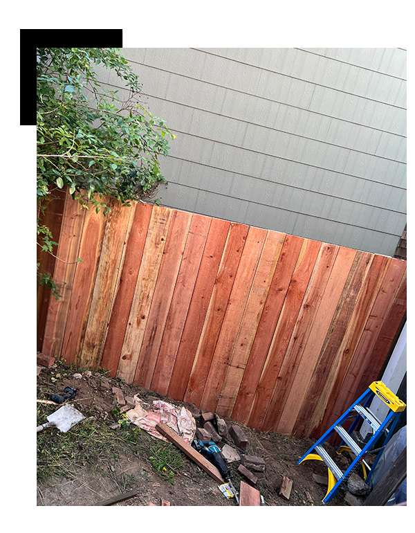 A newly installed wooden fence is seen beside a gray house and some greenery. Tools and materials are scattered on the ground, indicating ongoing construction. A blue ladder is also visible fence comapany near me.