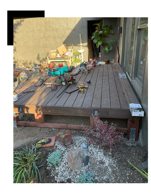 general-construction-contractor-San-Carlos-Ave-9-2-1_1 - JE Handyman Home Service A partially completed wooden deck with various construction tools and materials scattered on top. A potted plant and some garden items are visible in the background SF handyman.