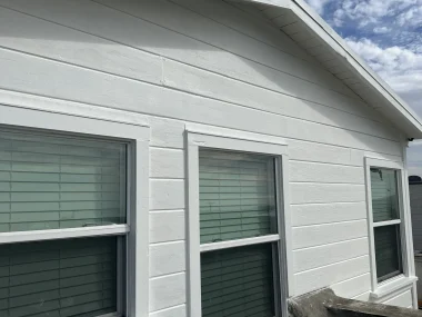 White building facade with three windows featuring green blinds, under a clear blue sky.